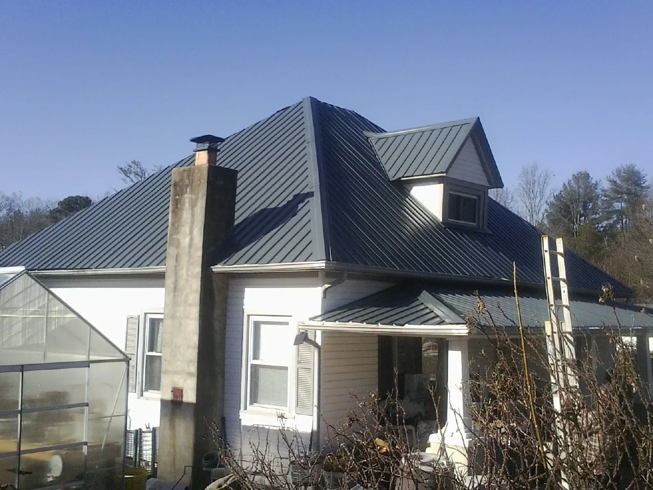 Dark blue standing seam metal roof on a white farmhouse with dormer — Slate & Tile Roof Repair by Roofing Brothers in Cooleemee