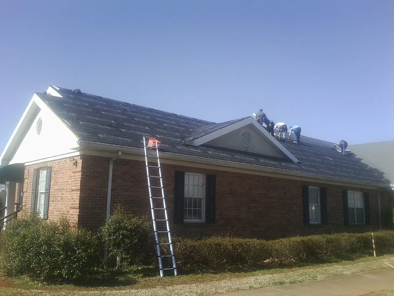 Crew tearing shingles off a brick ranch roof with a ladder set — Emergency Roof Repair work by our crew in Cooleemee
