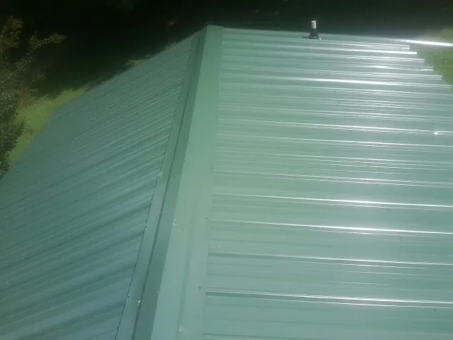New green metal panels meeting at the ridge of a roof — Flat Roof Repair work by our crew in Cooleemee
