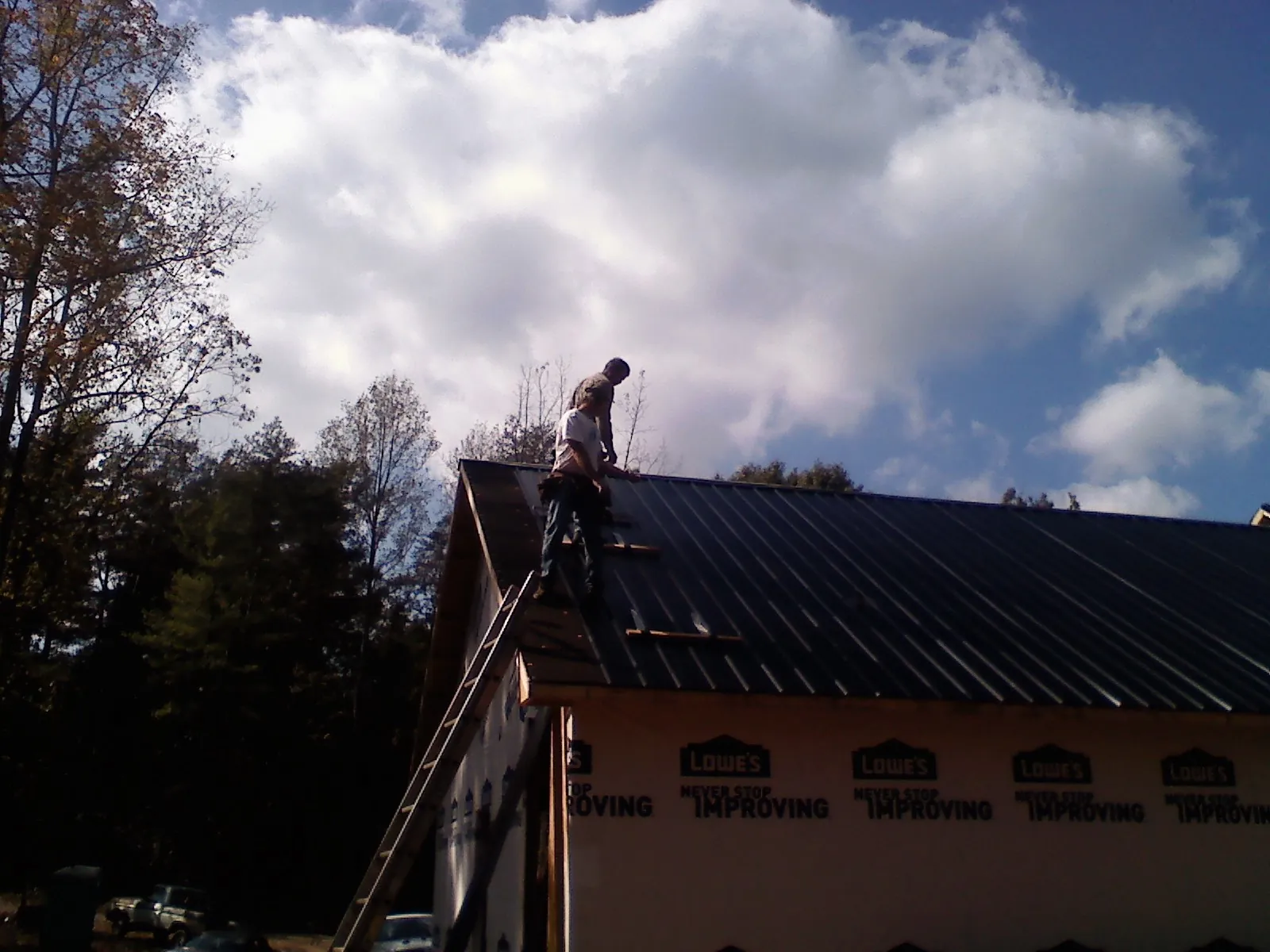 Roofer fastening dark metal panels high against a cloudy sky, from a Roof Inspection job in Cooleemee