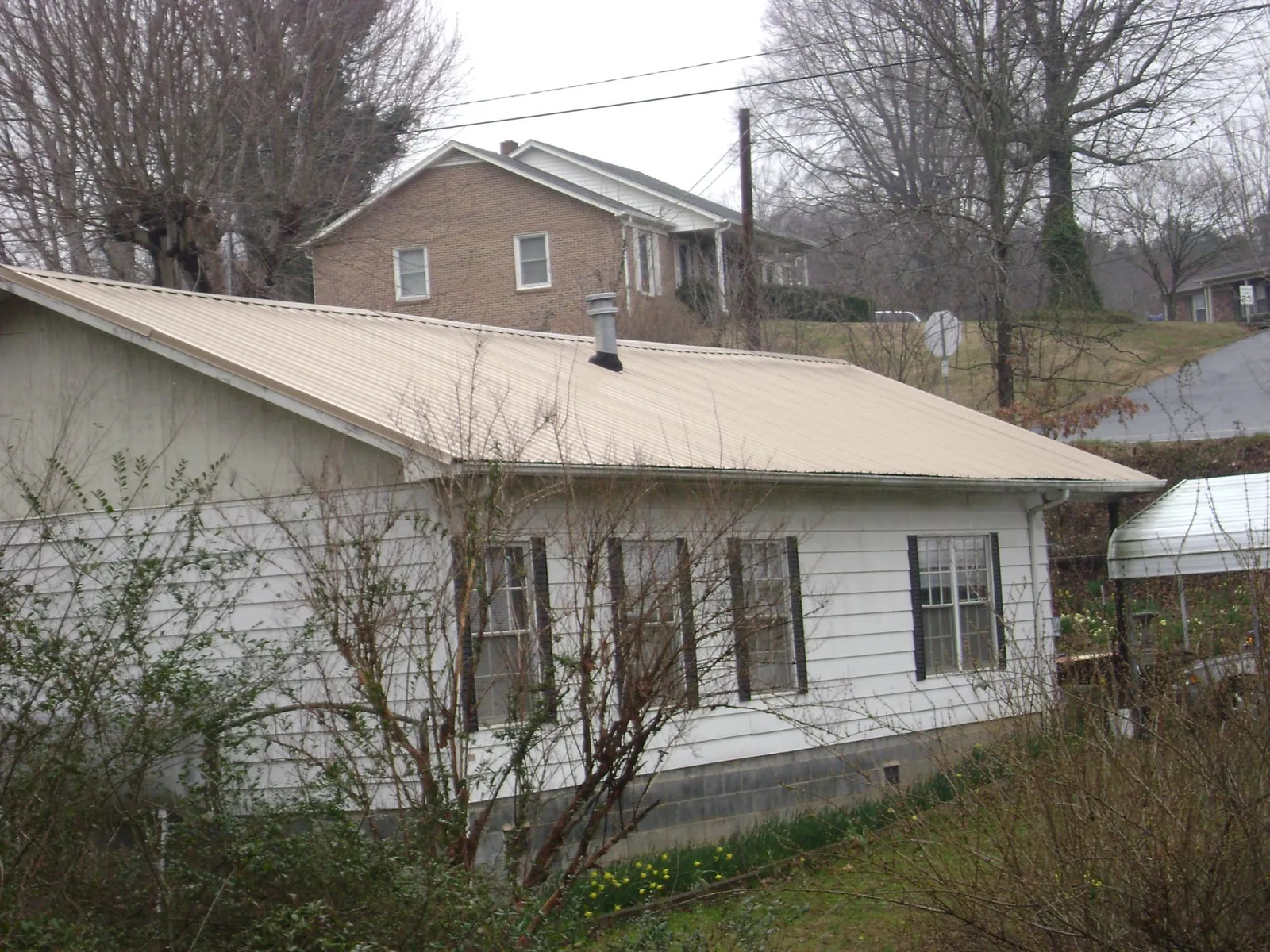 Tan metal roof on a white sided house set into a hillside — Commercial Roofing by Roofing Brothers in Cooleemee